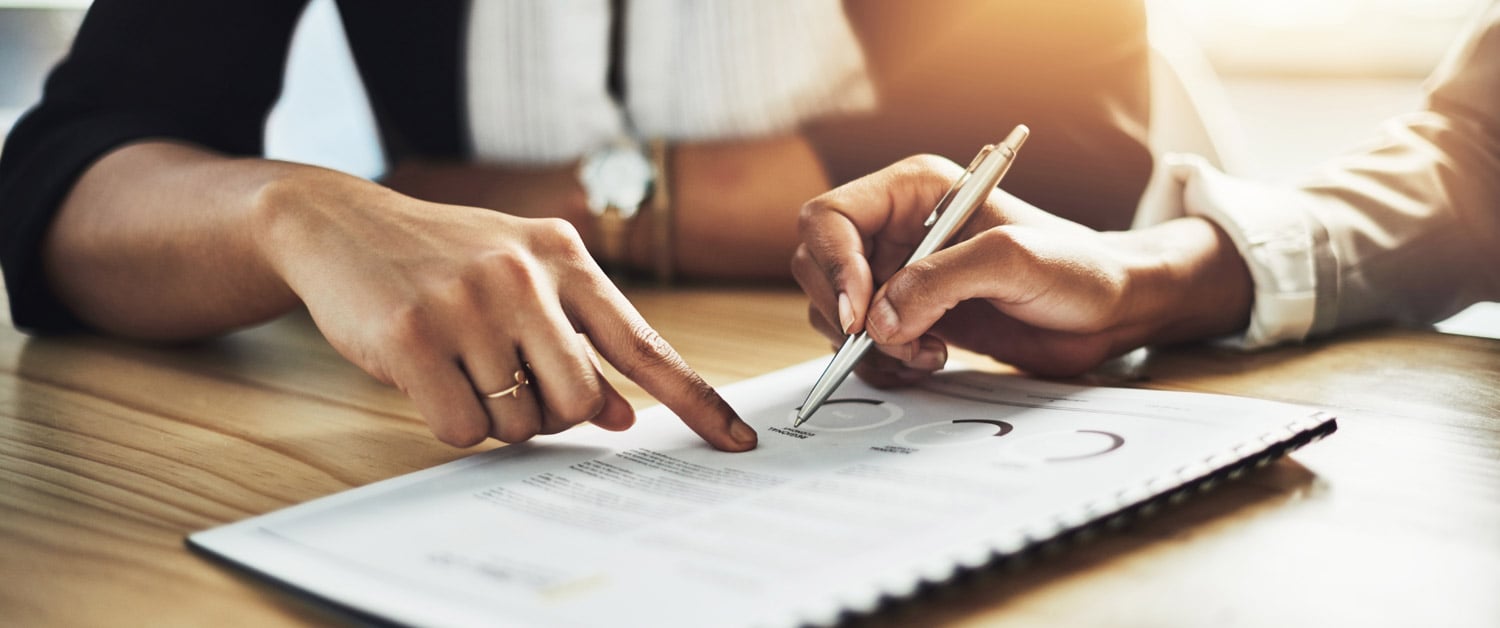 two people using pens to point to a word on a piece of paper