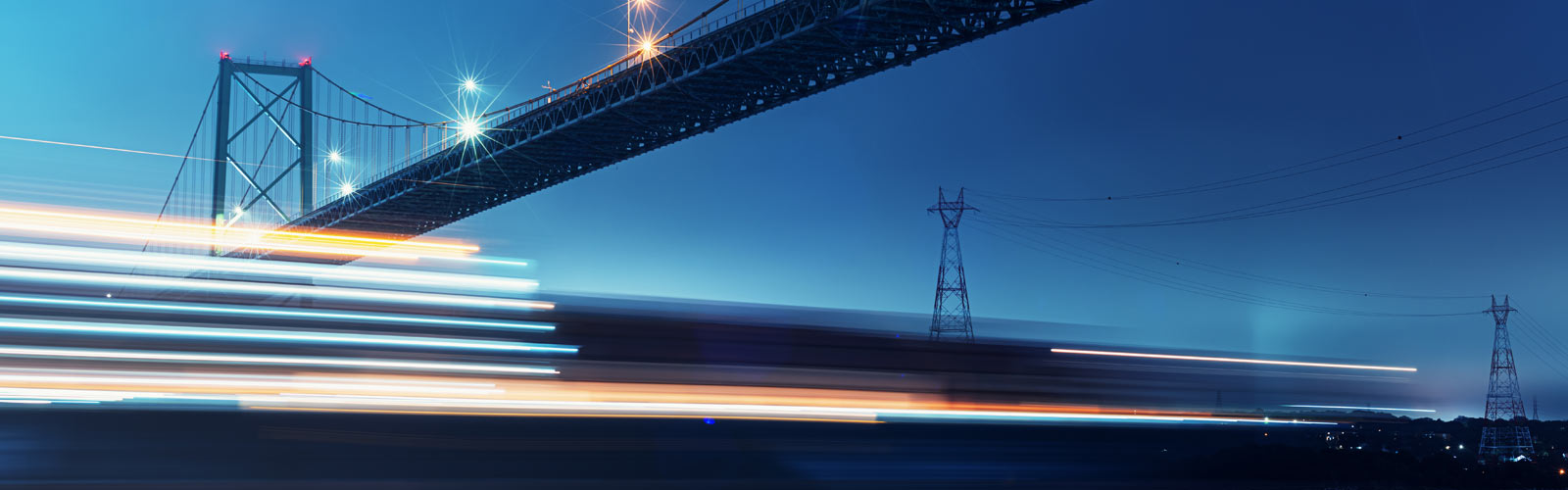 Blurred motion of ship passing under bridge with hydro towers in backgroun 